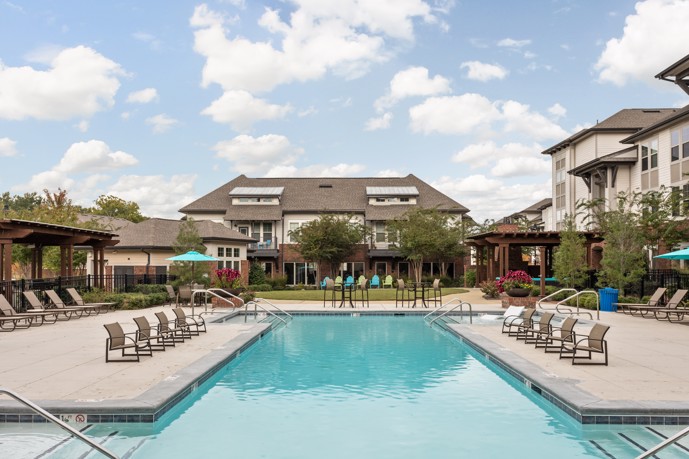 Swimming pool offering a generous sundeck, complete with lounge chairs and umbrellas, adjacent to the apartment buildings at Miller Creek at Germantown.
